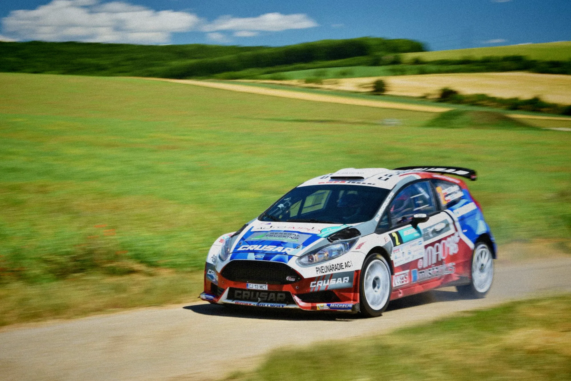 Pilote au volant d'une Ford Fiesta WRC franchissant à grande vitesse une route sinueuse des Vosges