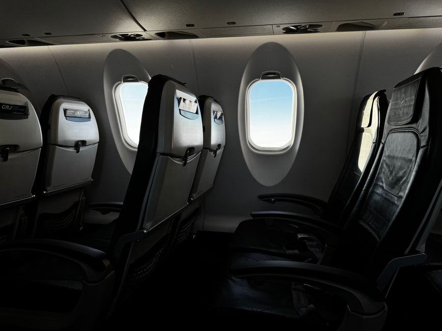 Interior of an empty airplane cabin with a bright sky visible through the window.
