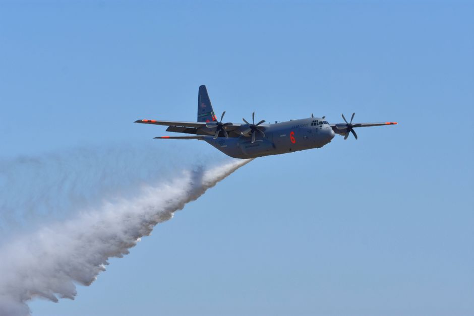 Aerial view of a firefighting aircraft dispersing water over a clear blue sky.