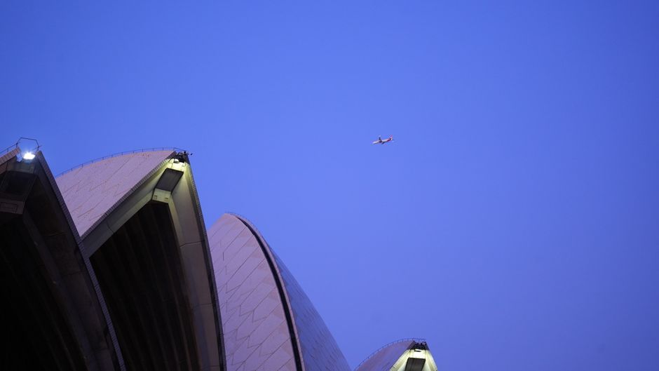Sydney Opera House under twilight sky with airplane flying above.