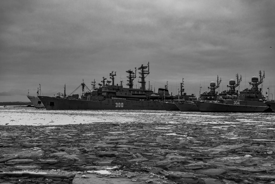 Black and white image of military ships frozen in an icy sea under a cloudy sky.