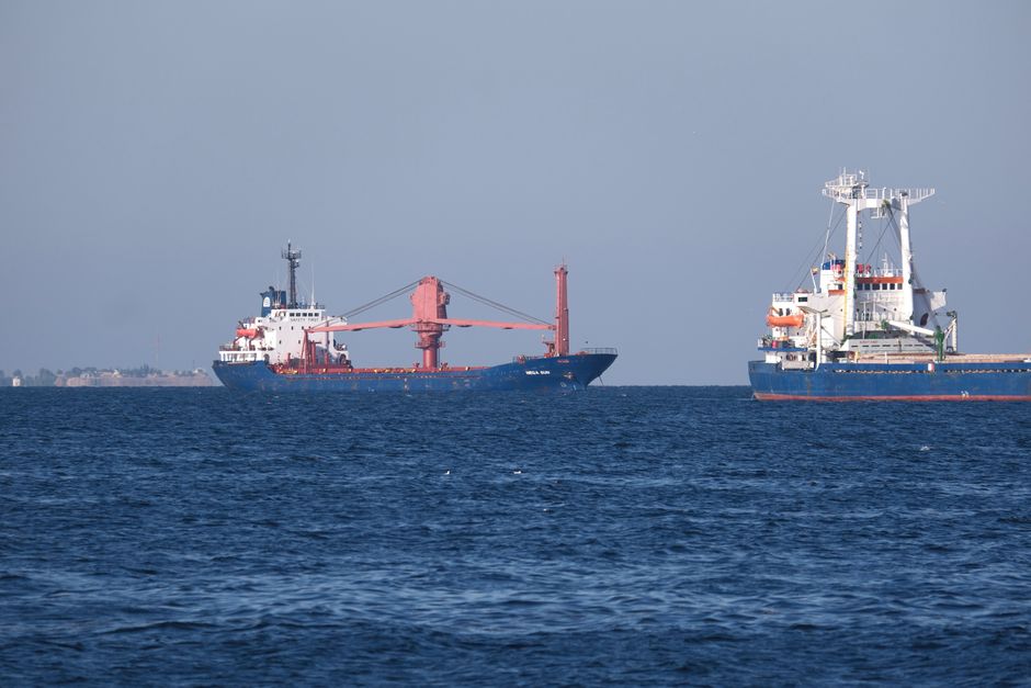 Two container ships sailing in the open sea, under a clear blue sky, captured in bright daylight.