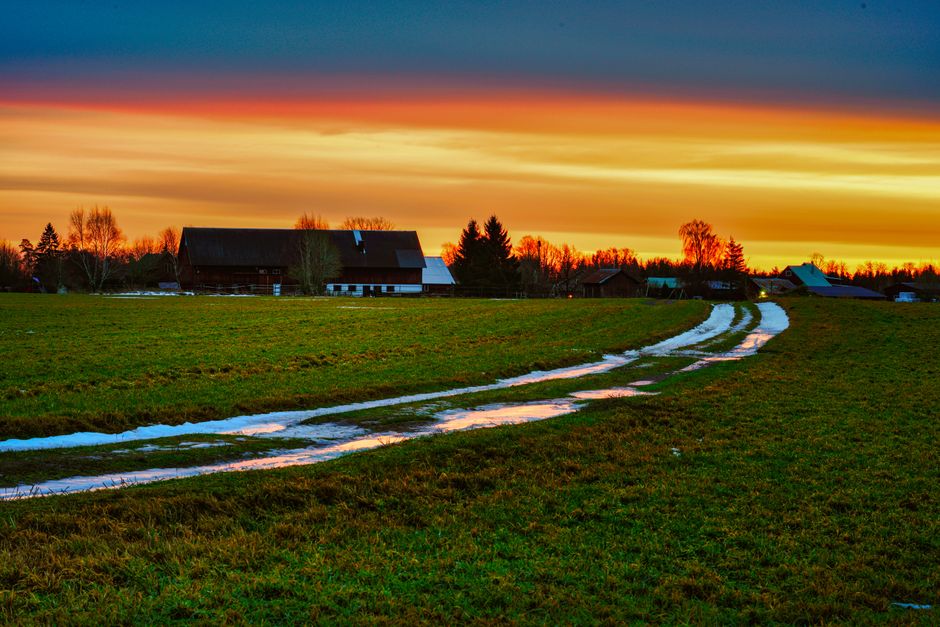 A beautiful sunset illuminates a rural farm with vibrant colors and a winding path.