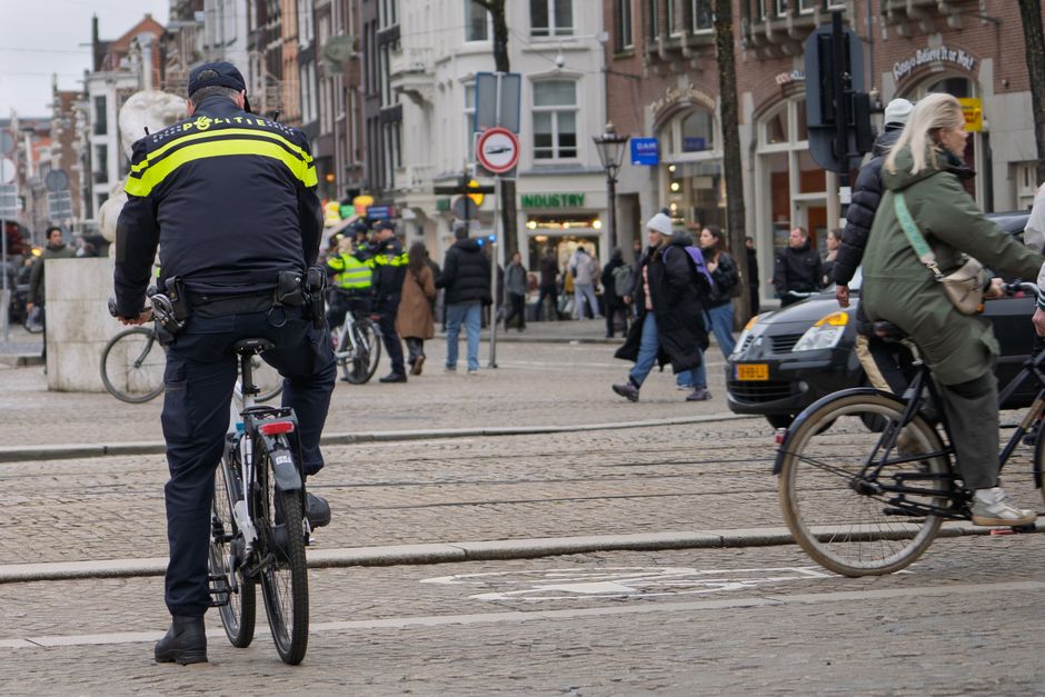 Police officer patrolling a busy city street on a bicycle, with pedestrians and cyclists around.