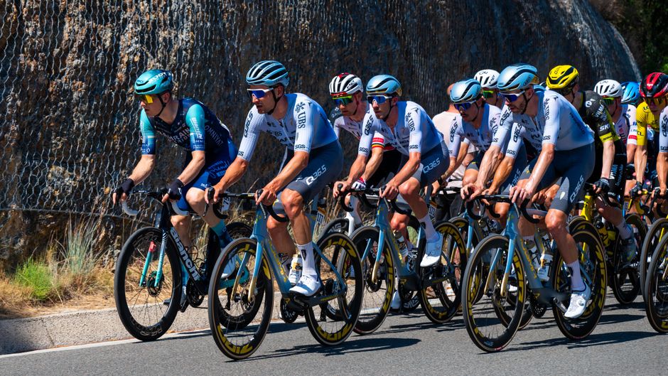A group of professional cyclists racing on a sunlit road, showcasing intense competition.