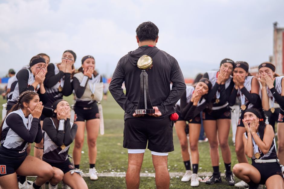 A victorious sports team celebrates with their coach holding a trophy on a field.