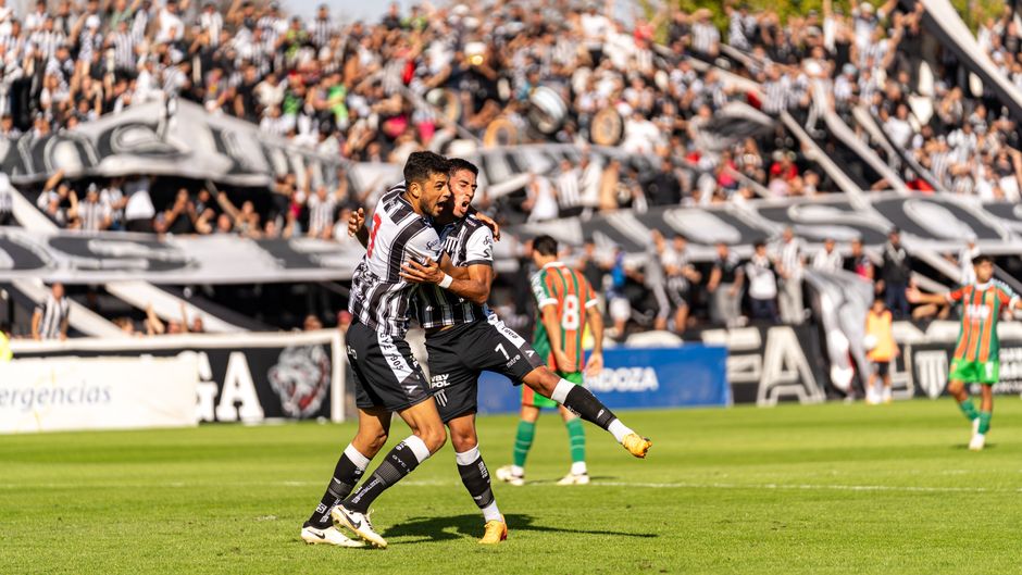 Football players celebrating a goal in a thrilling match with a cheering crowd.