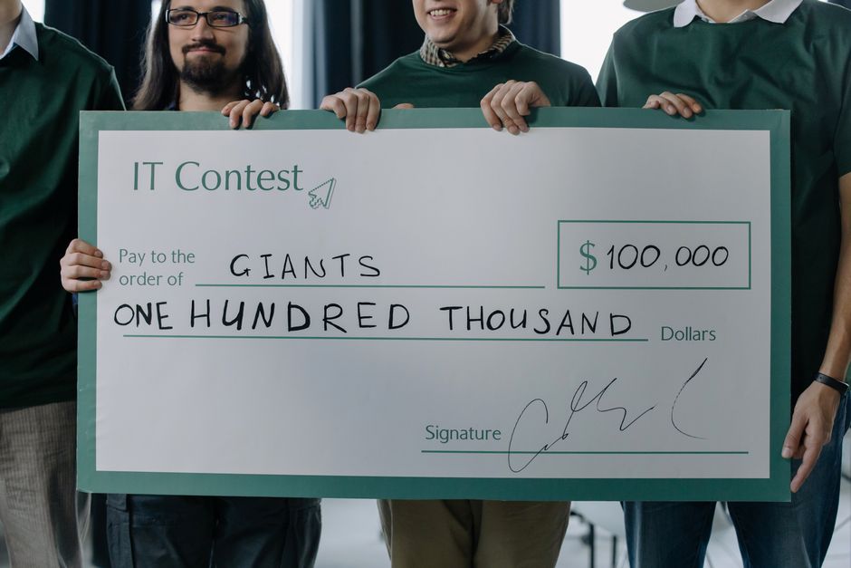 Group of men holding a 0,000 prize check after winning an IT contest.