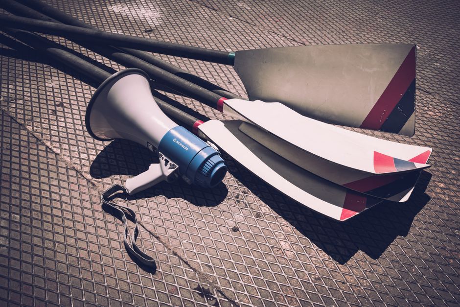 Close-up of a megaphone and rowing oars lying on a sunlit metal ground, showcasing sports gear.