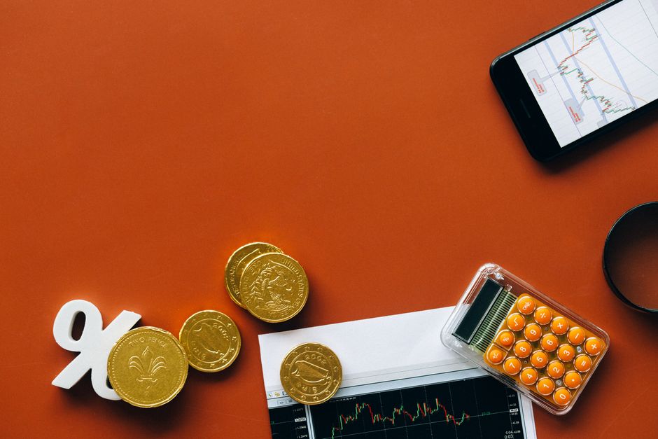 Flat lay showing coins, calculator, and charts on a red background for financial analysis and business concepts.