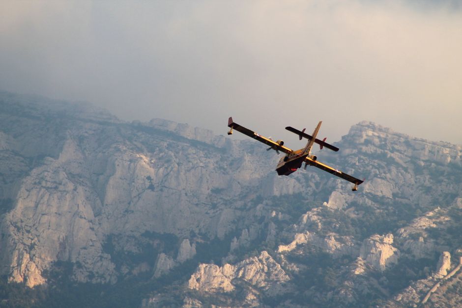 Aerial view of an airplane flying over rugged mountains during sunset, creating a dramatic silhouette.
