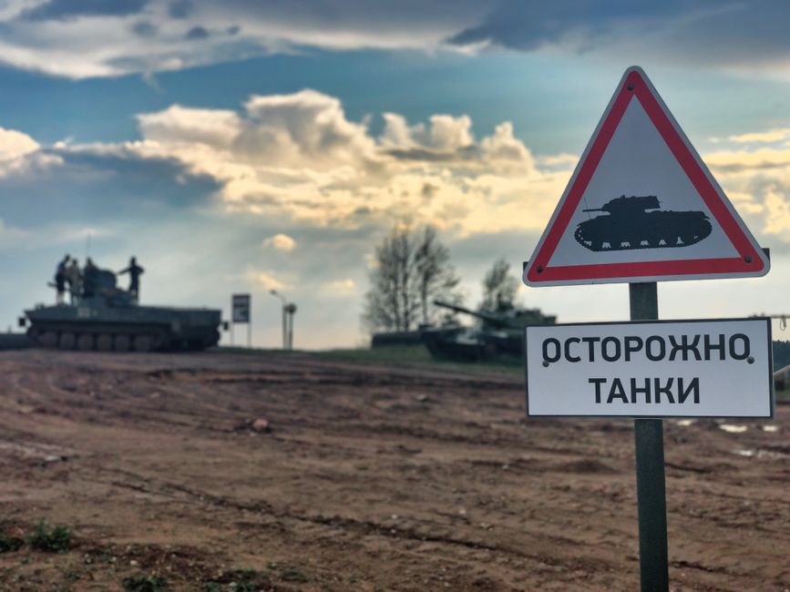 Military tanks in Belarus with a warning sign for caution on dirt road.