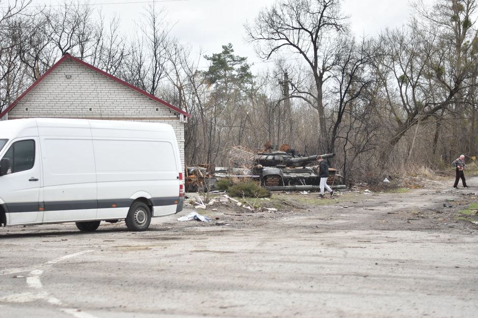 Scene of a war-torn area with an abandoned tank and van, illustrating the aftermath of conflict.