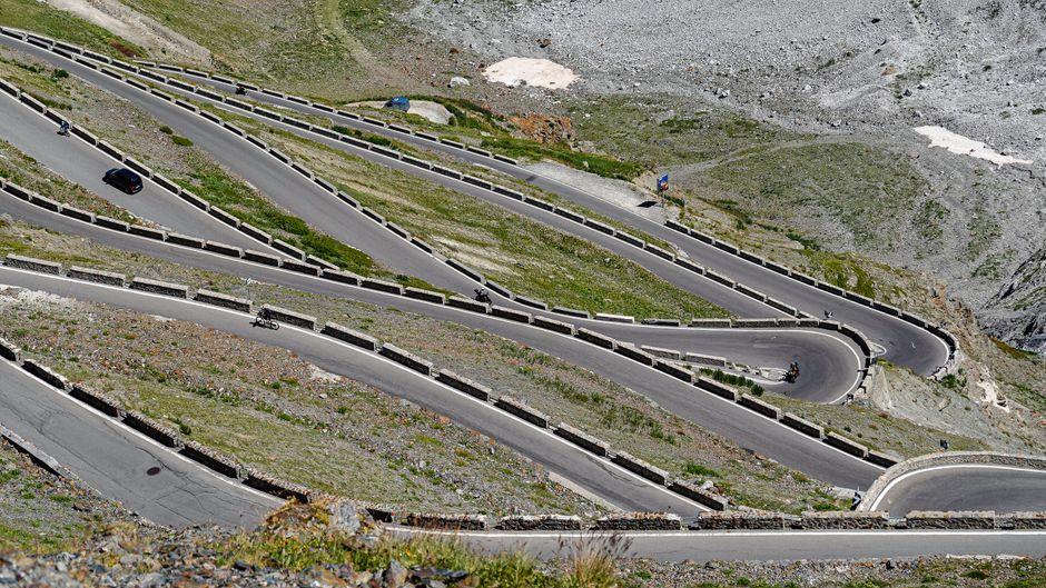 Aerial view of a winding mountain road with cyclists and a vehicle navigating sharp turns.