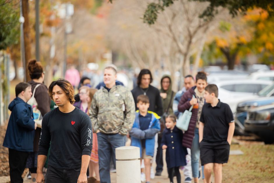 A diverse group of adults and children walking along a sidewalk in autumn.