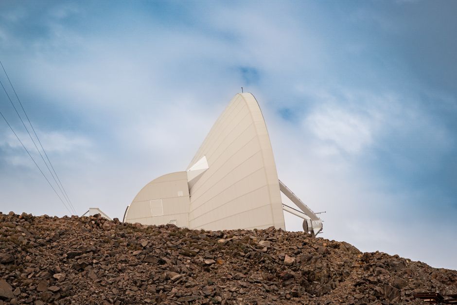 White observatory structure located on a rocky hill under a clear blue sky.