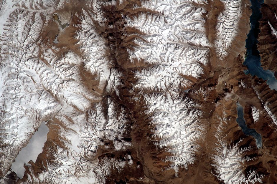 High-altitude view of mountain range with snow-capped peaks and rugged terrain.