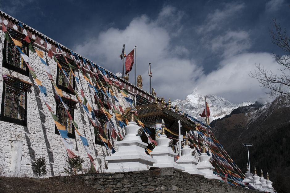 Colorful prayer flags adorn a Tibetan monastery against a mountain backdrop.