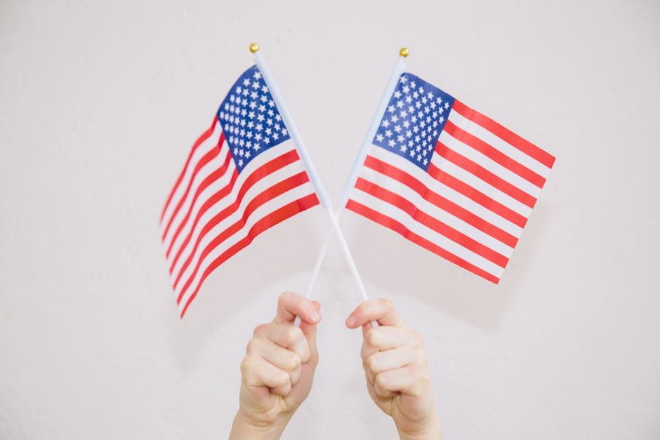 Two hands hold American flags against a white background symbolizing patriotism and freedom.