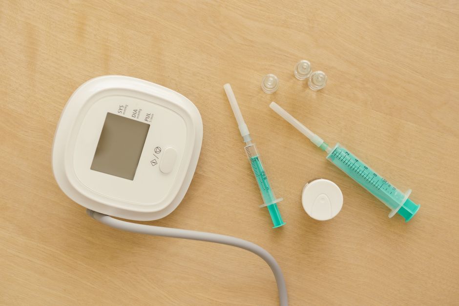 Flat lay of medical equipment including a sphygmomanometer and syringes on a wooden surface.