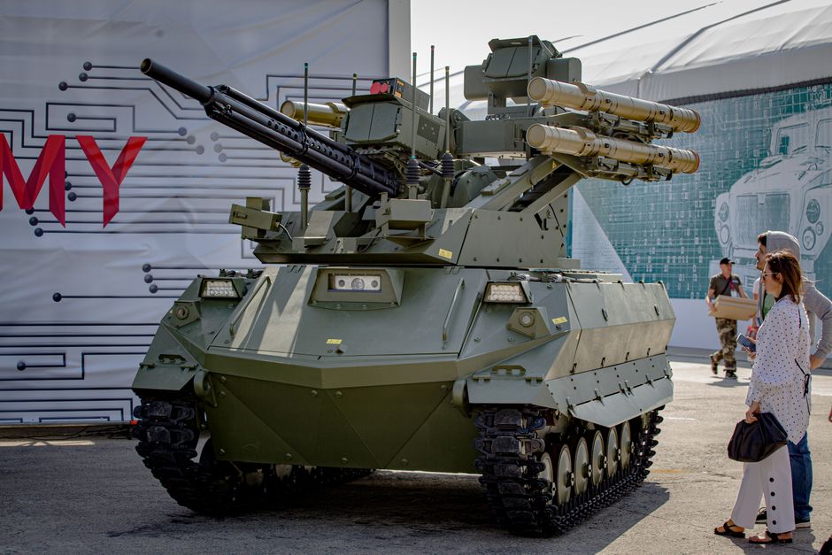 Green military tank with missile launchers on display outdoors with spectators.