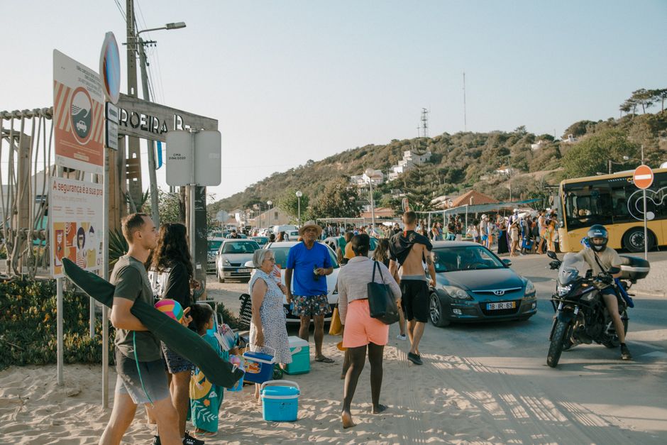 Busy scene at a beach entrance with people, cars, and a bus. Summer lifestyle captured.