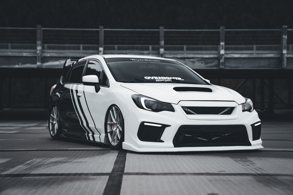 Stylish white sports car with black stripes parked outdoors, featuring custom modifications.