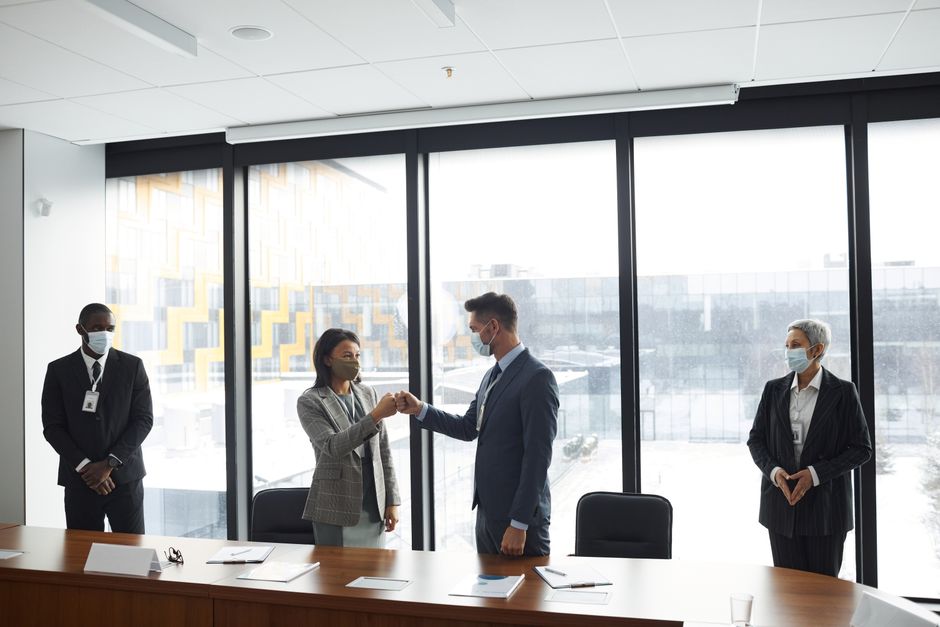 Diverse professionals in formal attire fist bumping at a business meeting in a conference room.
