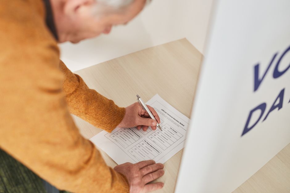 Senior man marking a ballot at a voting booth in an indoor polling station.