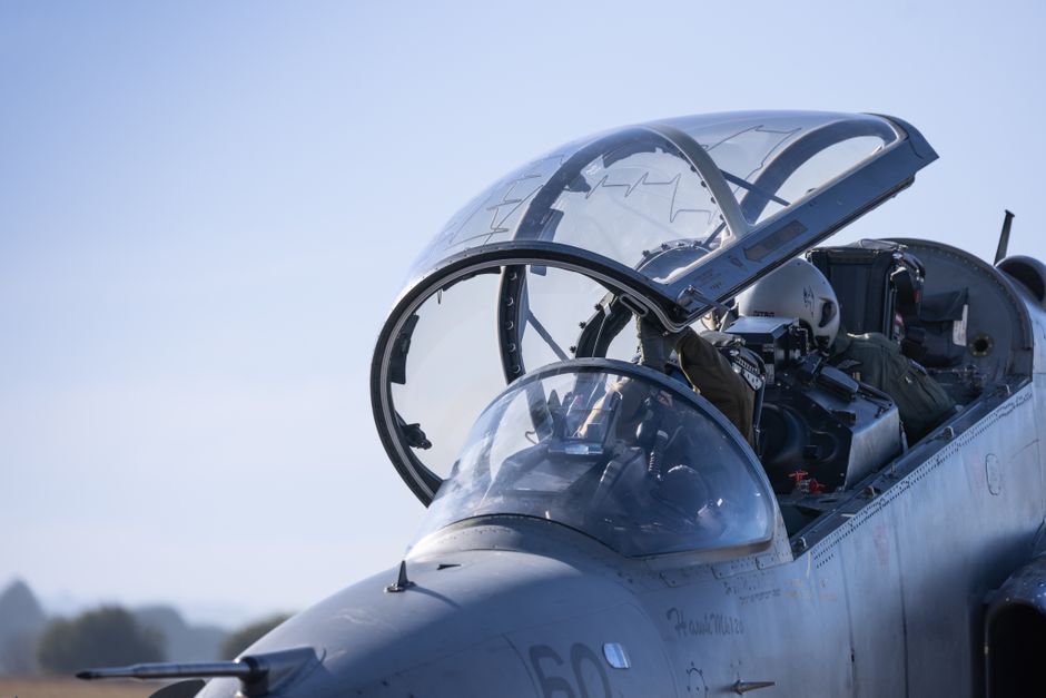 Detailed view of a military jet cockpit with pilots preparing for flight against a clear sky.