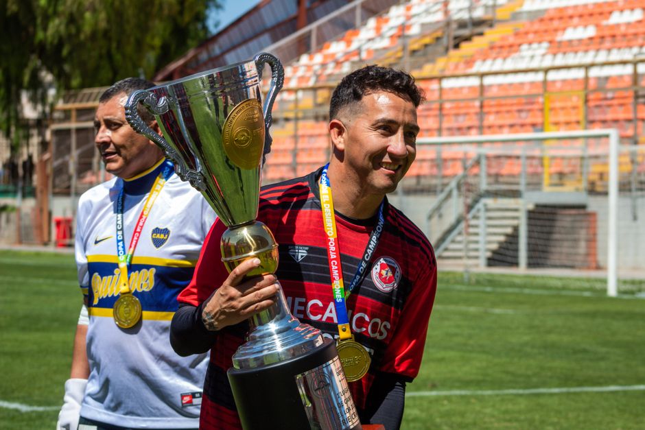 Two soccer players celebrate with a championship trophy on the field.