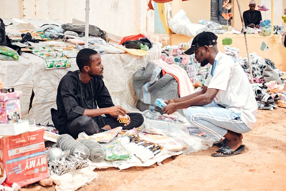 Two street vendors negotiate over goods at an outdoor market filled with various items for sale.