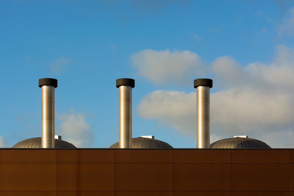 Three industrial chimneys reach into a serene blue sky dotted with clouds.