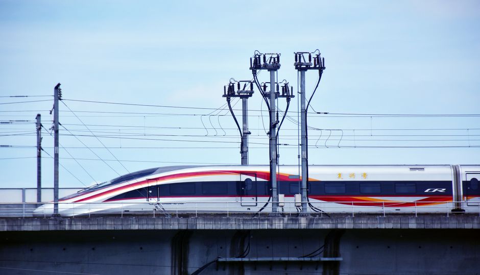 A sleek high-speed train travels along an elevated track on a clear day.