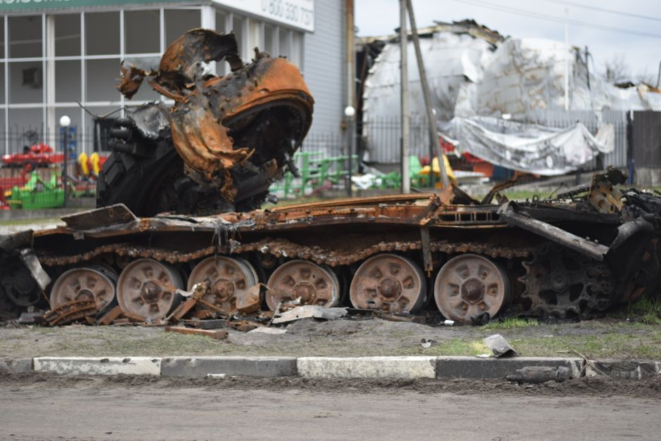 A rusted and damaged military tank lies abandoned on a city street.
