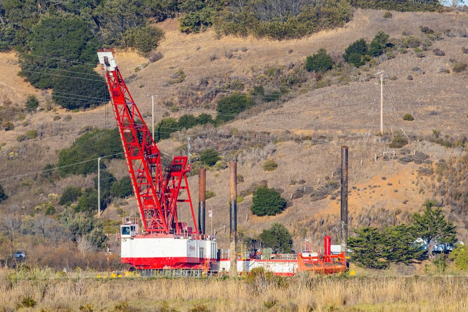 Large red crane at a construction site in a hilly rural landscape.