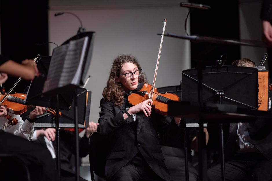 Violinist in a live classical orchestra performance playing with passion on stage.