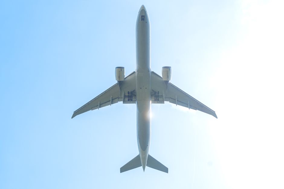 A commercial airplane captured from below, soaring against a bright blue sky.