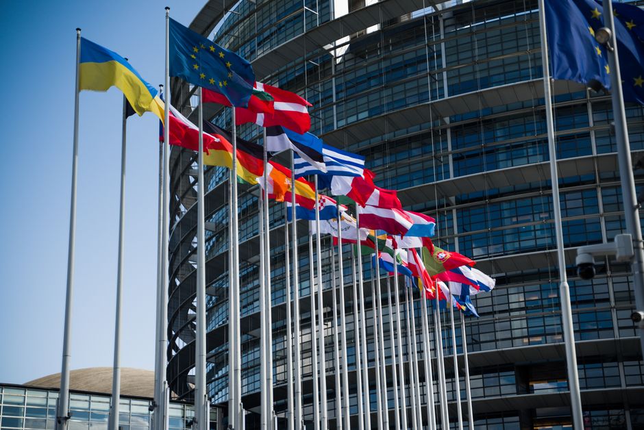 Flags of European Union countries outside a modern building facade.