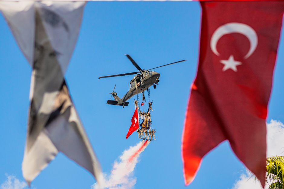 A military helicopter performs an aerial display with soldiers and Turkish flags in Istanbul, Türkiye.