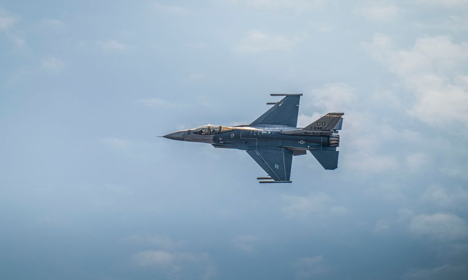 Military F-16 jet flying against a backdrop of clouds, showcasing aviation power.