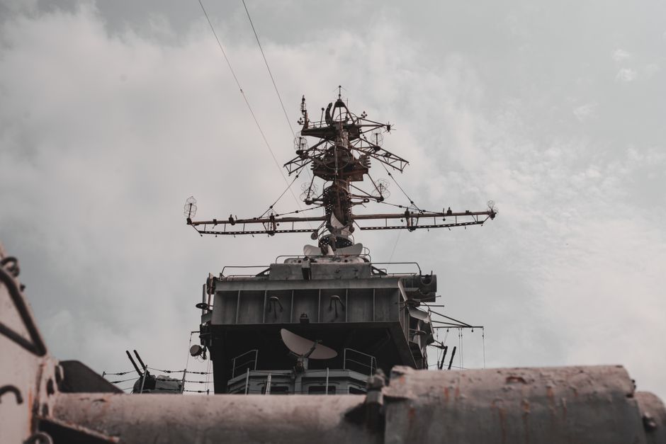Close-up view of a military warship's radar and antenna mast against a cloudy sky.