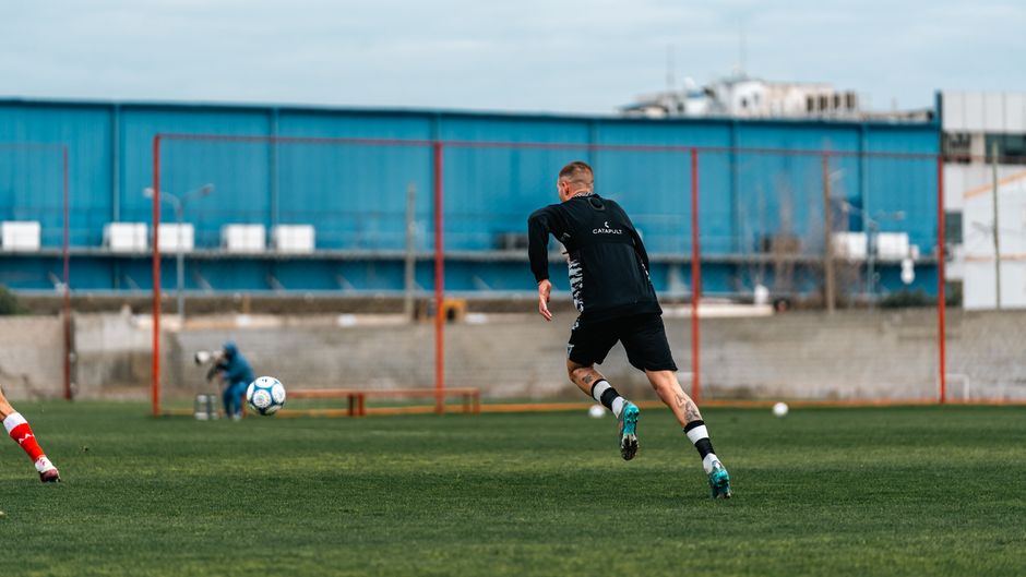 Male soccer player in training session, running towards the ball on a field.