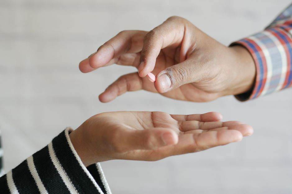 Close-up of hands exchanging a single pill, symbolizing medication sharing.