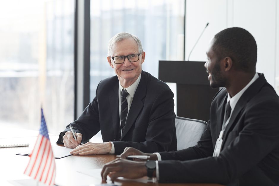 Two business professionals discussing and signing documents at a meeting with an American flag on the table.