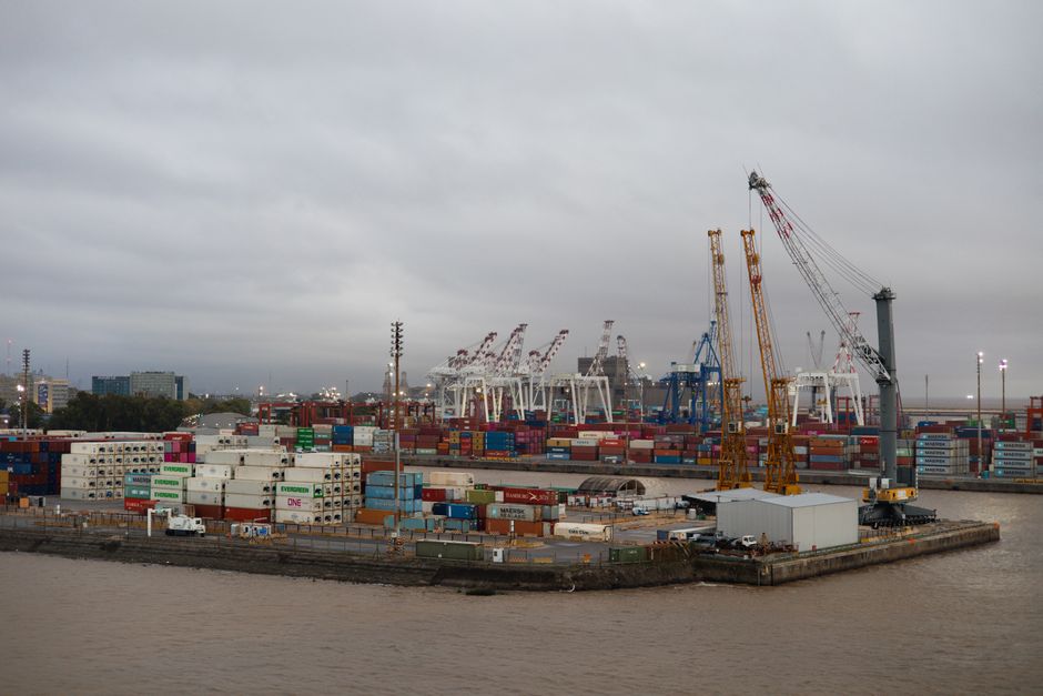 Expansive view of a busy industrial port with shipping containers and cranes under cloudy skies.