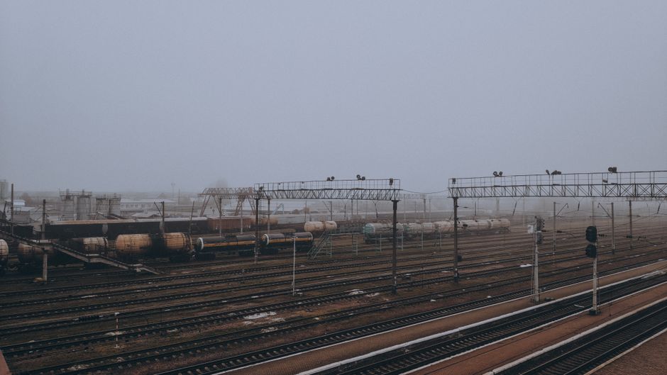 Moody winter scene of a foggy train station with tank wagons, tracks, and mist.