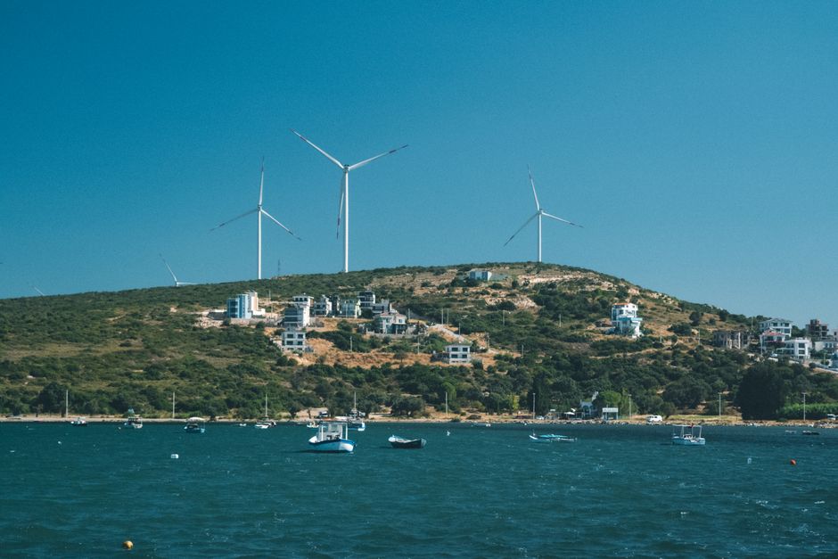 Wind turbines on a coastal hill overlooking the sea on a clear day, showcasing alternative energy and natural beauty.