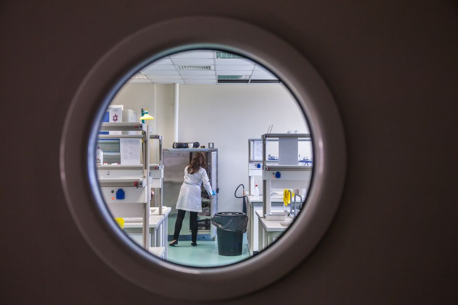 A female scientist in a lab coat working inside a state-of-the-art laboratory through a circular window view.