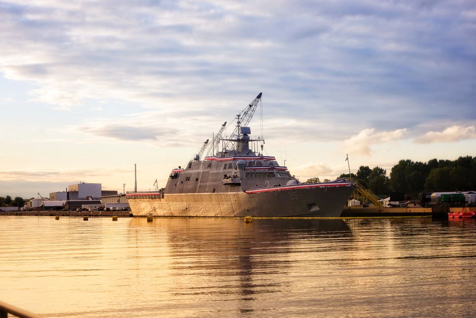 A warship docked in a serene harbor in Marinette, WI, during a golden sunset.